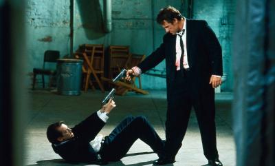 A still from the film Reservoir Dogs - two men in suits point guns at one another in an intense face off.