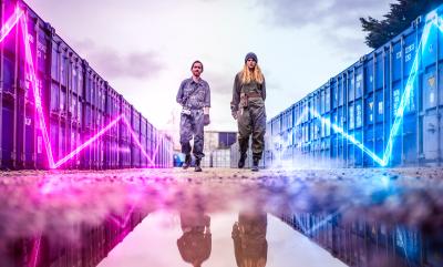 Two People Stood Behind A Puddle With Blue And Pink Light Lines Flowing Towards Them