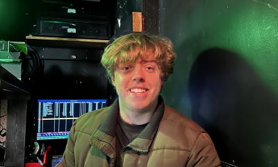 A Man Sat In A Technical Box With Computer Screens