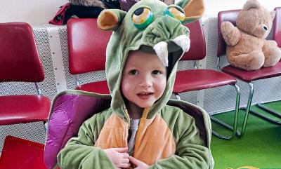 A boy dressed up as a dragon, surrounded by lots of toys